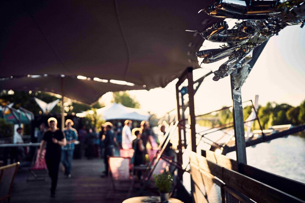 Gäste sitzen im Open‑Air‑Bereich von Fridas Pier am Neckar während eines Corporate Events in sommerlicher Atmosphäre.