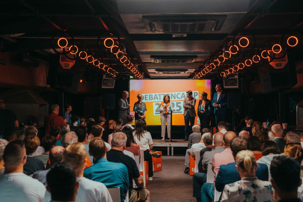 Reihenbestuhlung im Unterdeck von Fridas Pier mit Bühne und Präsentationsfläche in industrieller Atmosphäre.